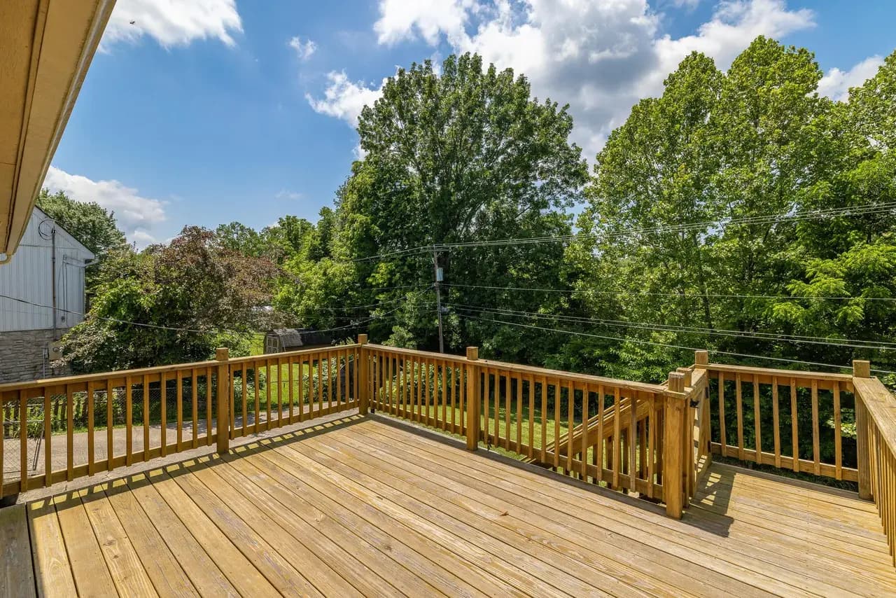 Deck before: bare pressure-treated boards with a wood spindle railing blocking the view of the trees.