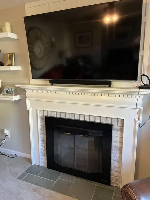 The same fireplace after: whitewashed brick with the texture still showing, black doors, and floating shelves on the wall beside it.