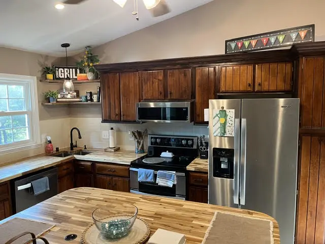 The same kitchen after: butcher block countertops, darker restained cabinets, open shelving, a black faucet, and a butcher block island.