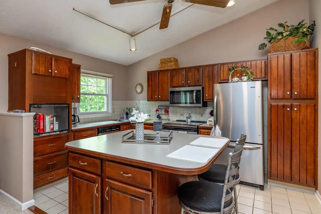 Kitchen before the work: oak cabinets, white laminate countertops, a white laminate island with stools, and a vaulted ceiling.