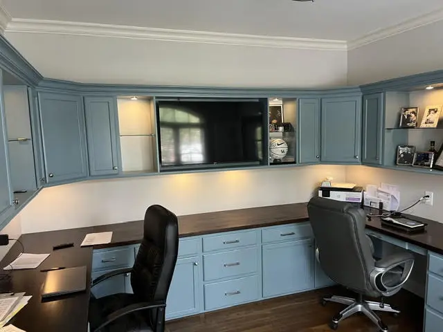 A television mounted on the wall between two runs of built-in office cabinetry.