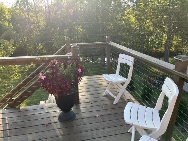 The refinished deck at the end of the day, with the cable railing and the tree line behind it.
