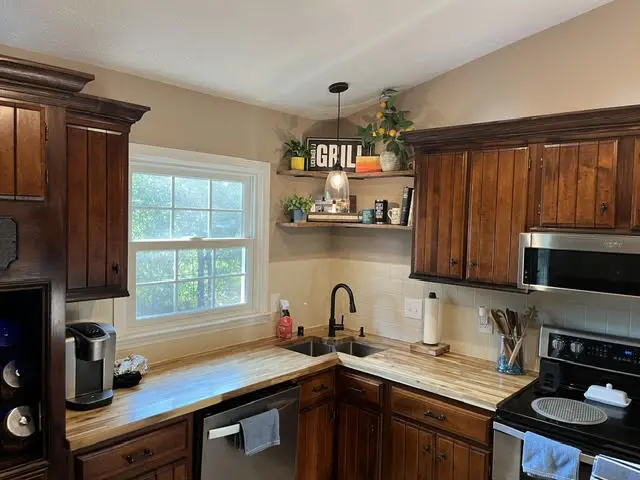 The sink corner after: butcher block counter, a deep sink with a black faucet, an open shelf above, and lighting under the cabinets.
