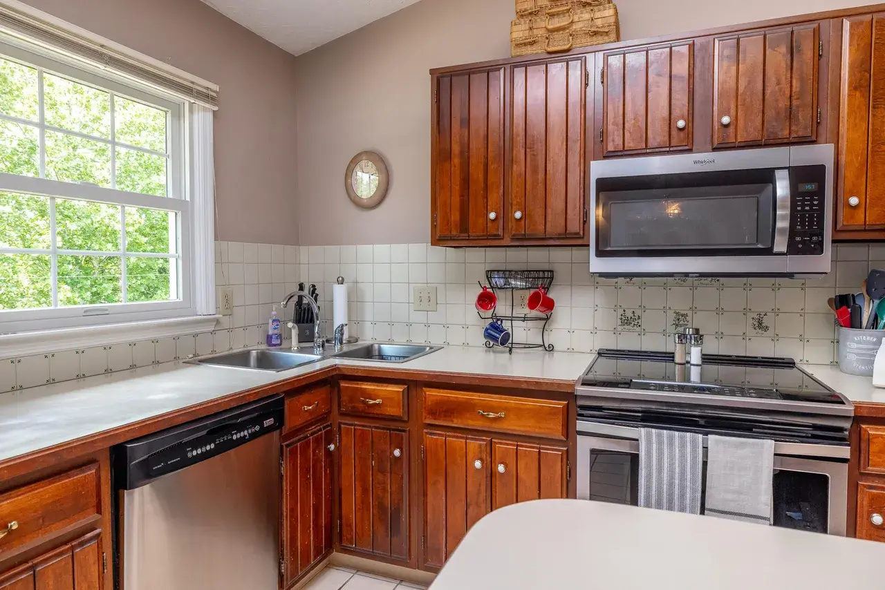 The sink corner before: white laminate counter, tile backsplash, and a chrome faucet under the window.