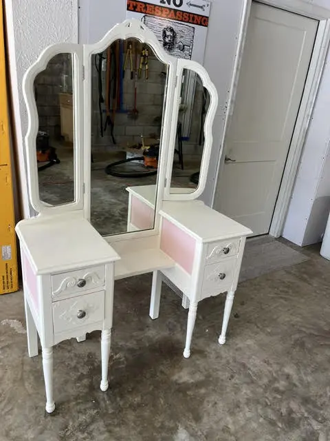 The same dressing table from the front, with blush-pink drawer fronts against the white frame.